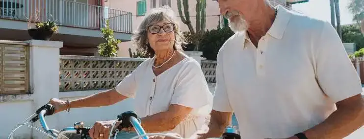 An older couple with bicycles standing together outdoors on a sunny day