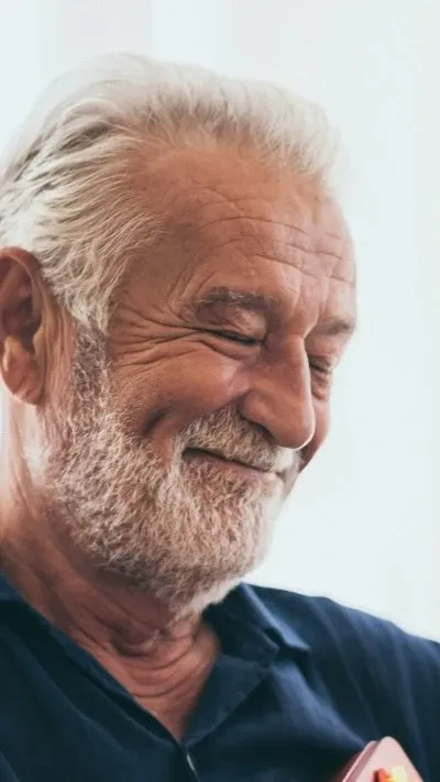 Close-up portrait of an older man with gray hair, a beard, and a warm smile with his eyes gently closed